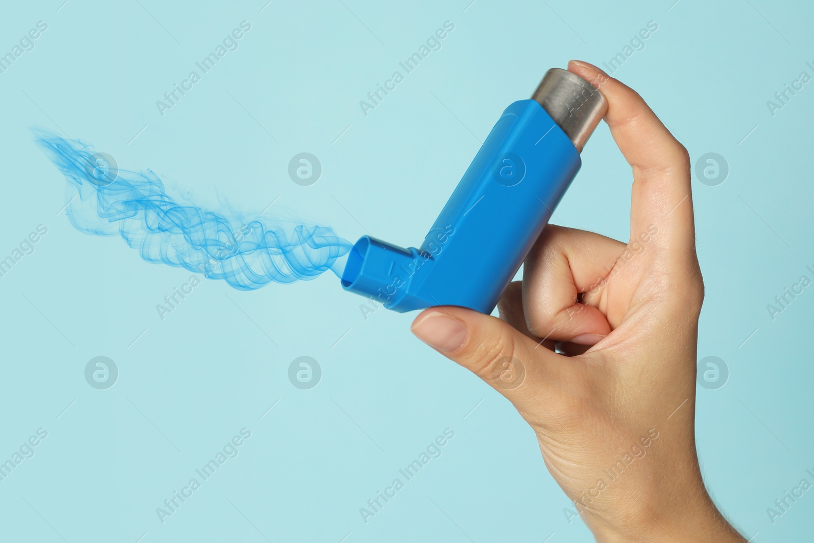 Image of Asthma treatment. Woman holding inhaler on light blue background, closeup. Aerosolized medication coming out of device