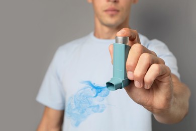 Asthma treatment. Man holding inhaler on grey background, closeup. Aerosolized medication coming out of device