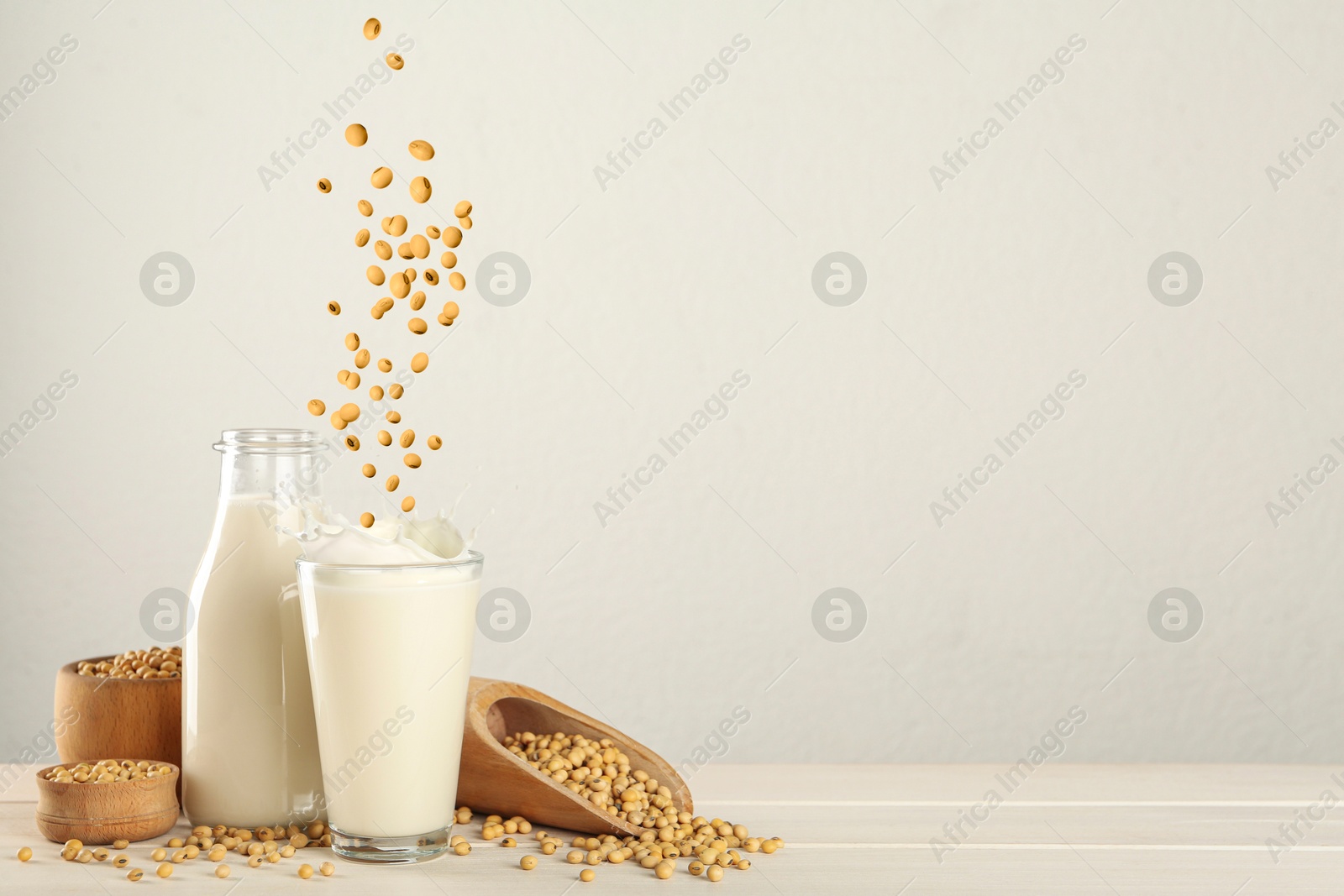 Image of Soy beans falling into glass of plant milk on white table. Space for text