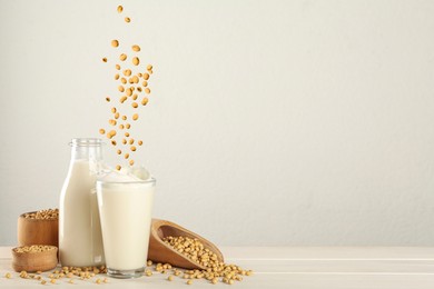 Image of Soy beans falling into glass of plant milk on white table. Space for text