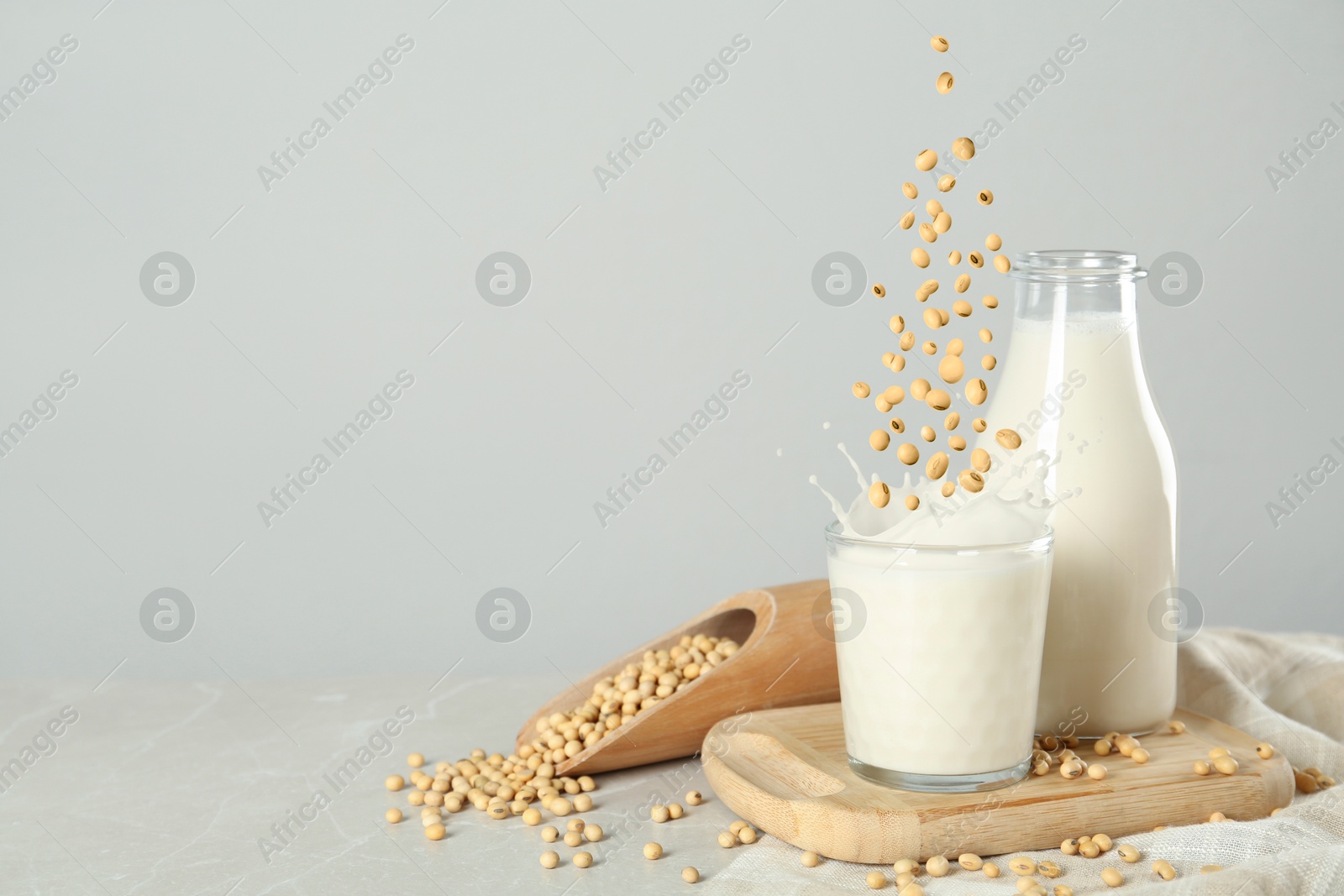 Image of Soy beans falling into glass of plant milk on grey table. Space for text