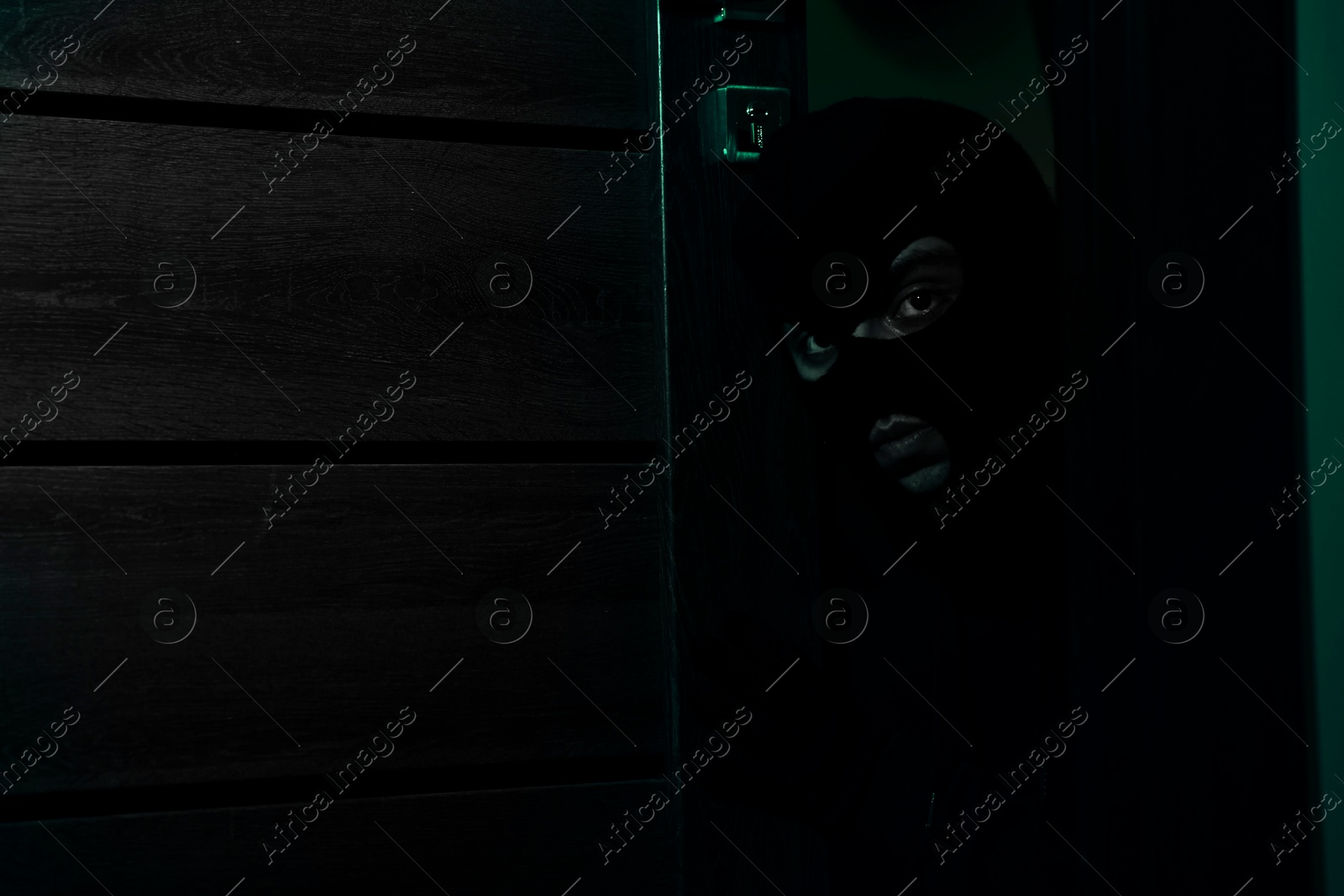 Image of Thief in balaclava entering house at night, toned in green. Robbery