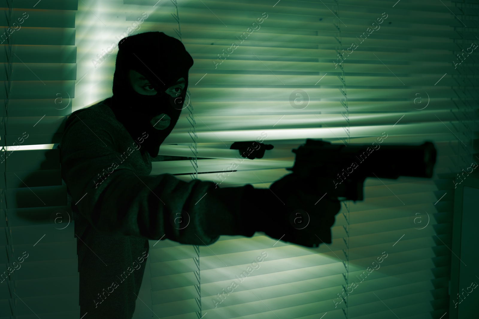 Image of Thief with gun coming out of blinds at night, toned in green. Armed robbery