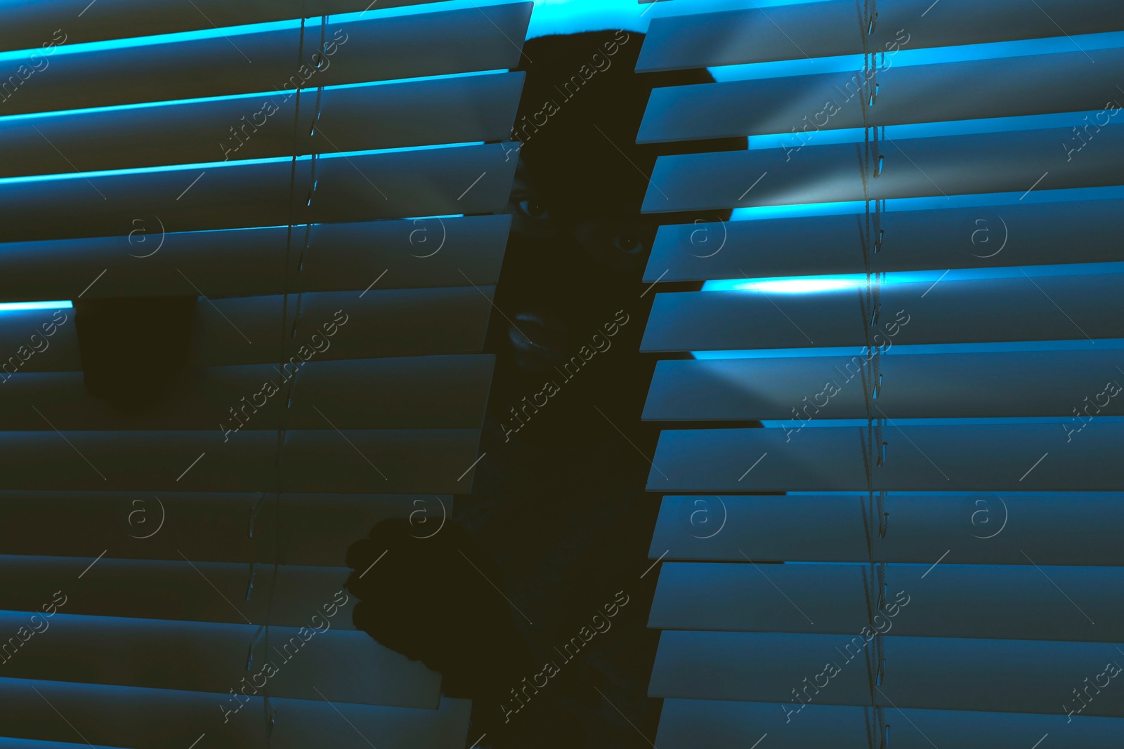 Image of Thief looking out of blinds at night. Robbery