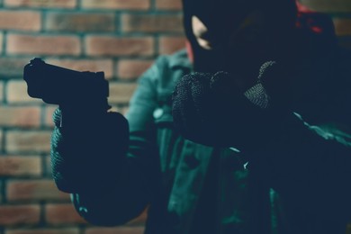 Image of Dangerous criminal with gun near brick wall, selective focus. Armed robbery