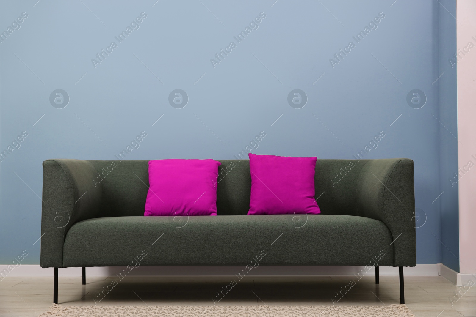 Image of Comfortable sofa with magenta color cushions near light blue wall in room