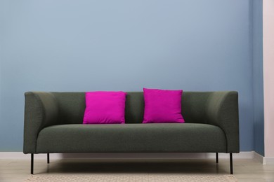 Image of Comfortable sofa with magenta color cushions near light blue wall in room