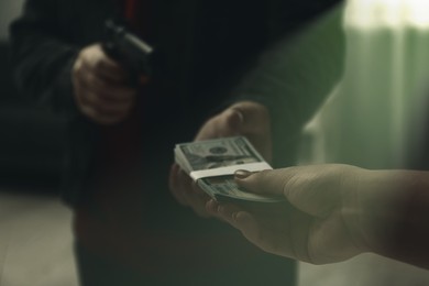 Image of Woman giving money to criminal with gun indoors, closeup. Armed robbery