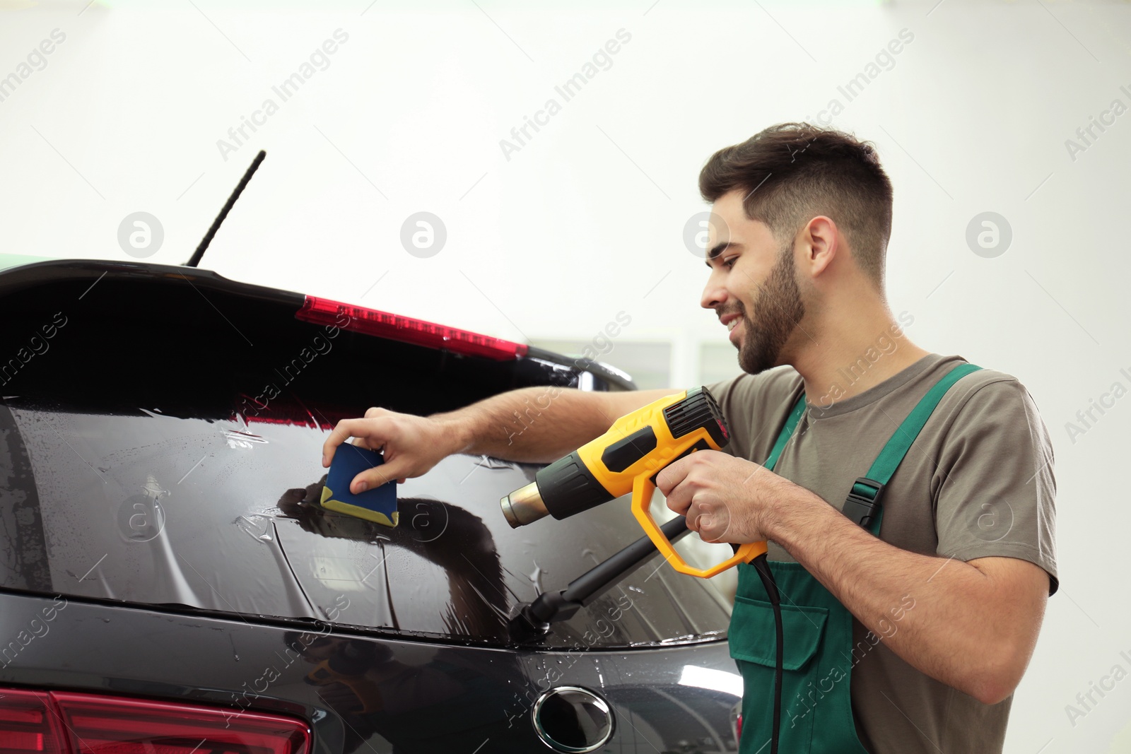 Photo of Worker tinting car window with heat gun in workshop