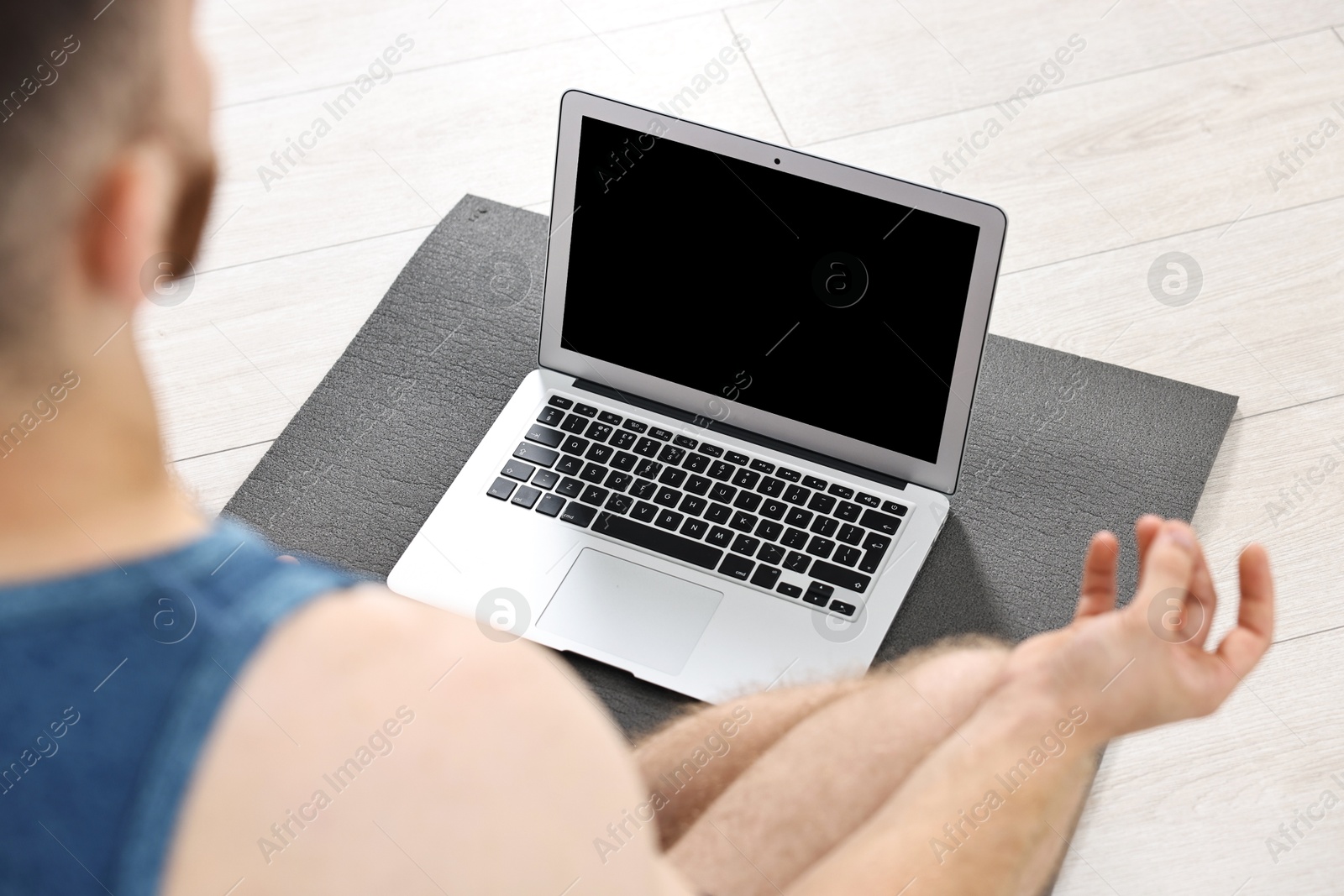 Photo of Man meditating near laptop on yoga mat at home, closeup