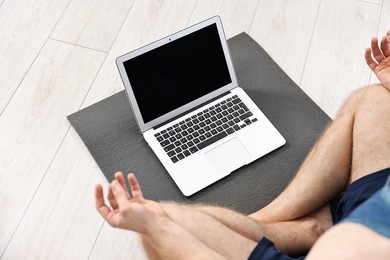 Man meditating near laptop on yoga mat at home, closeup