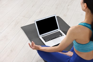 Woman meditating near laptop on yoga mat at home, closeup. Space for text