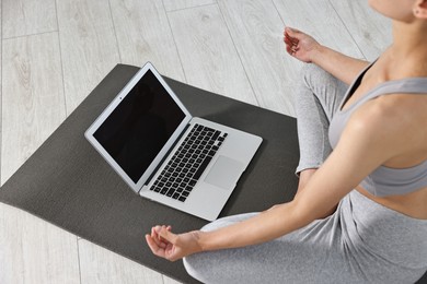 Woman meditating near laptop on yoga mat at home, closeup