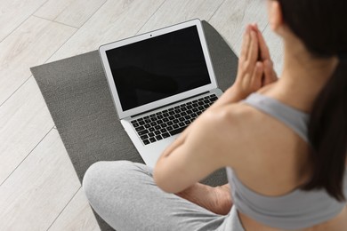 Woman meditating near laptop on yoga mat at home, closeup