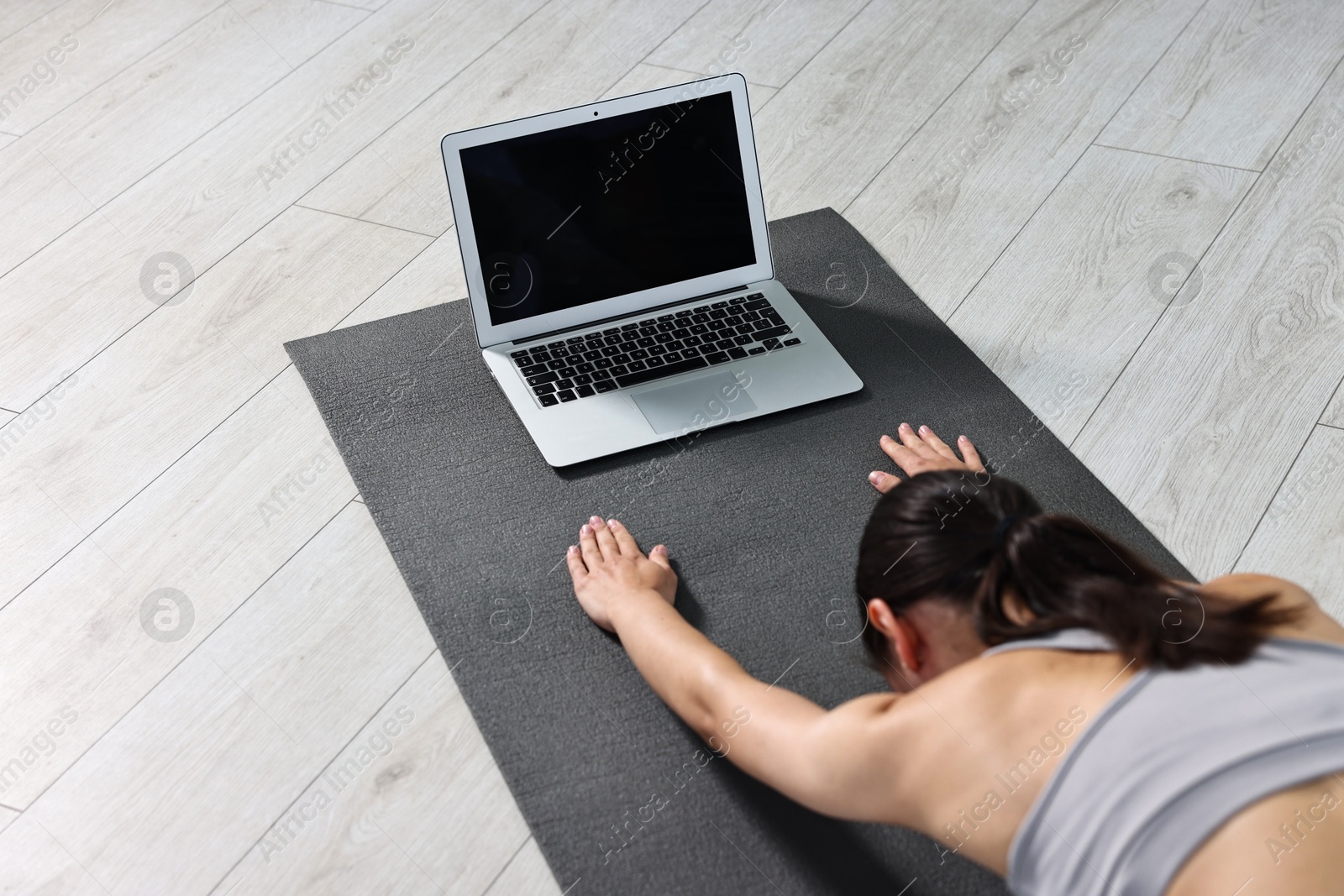 Photo of Woman practicing yoga near laptop on mat at home