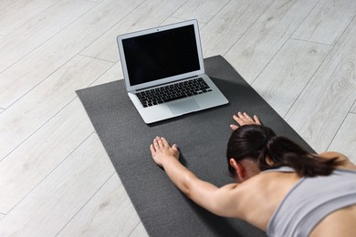 Woman practicing yoga near laptop on mat at home