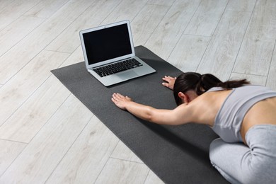 Photo of Woman practicing yoga near laptop on mat at home