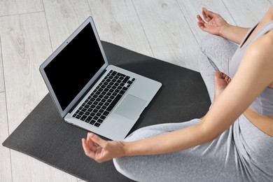 Photo of Woman meditating near laptop on yoga mat at home, closeup