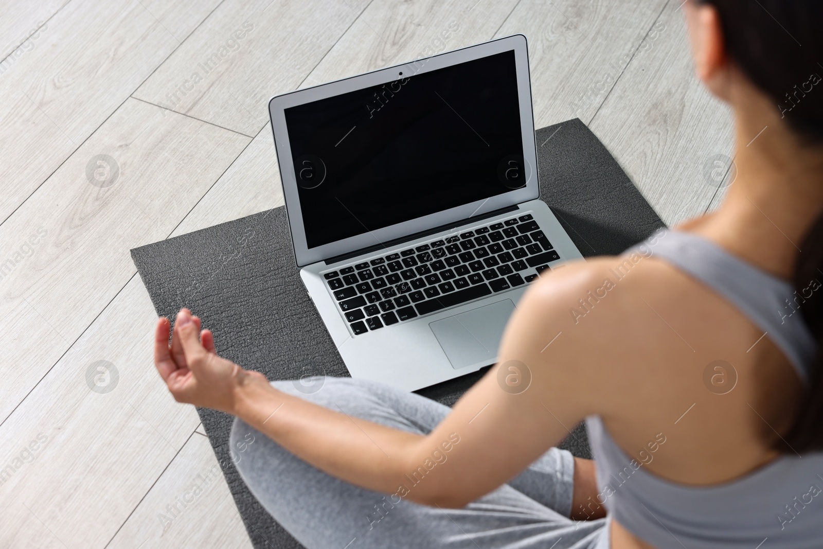 Photo of Woman meditating near laptop on yoga mat at home, closeup