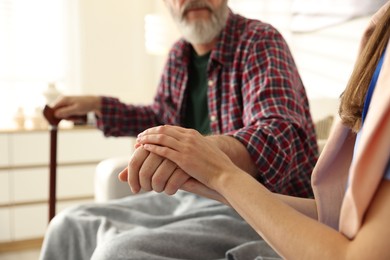 Photo of Caregiver supporting senior man on sofa indoors, closeup. Home health care service