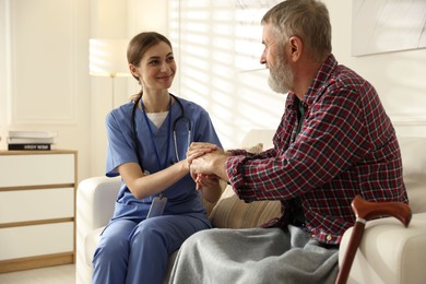 Caregiver supporting senior man on sofa. Home health care service