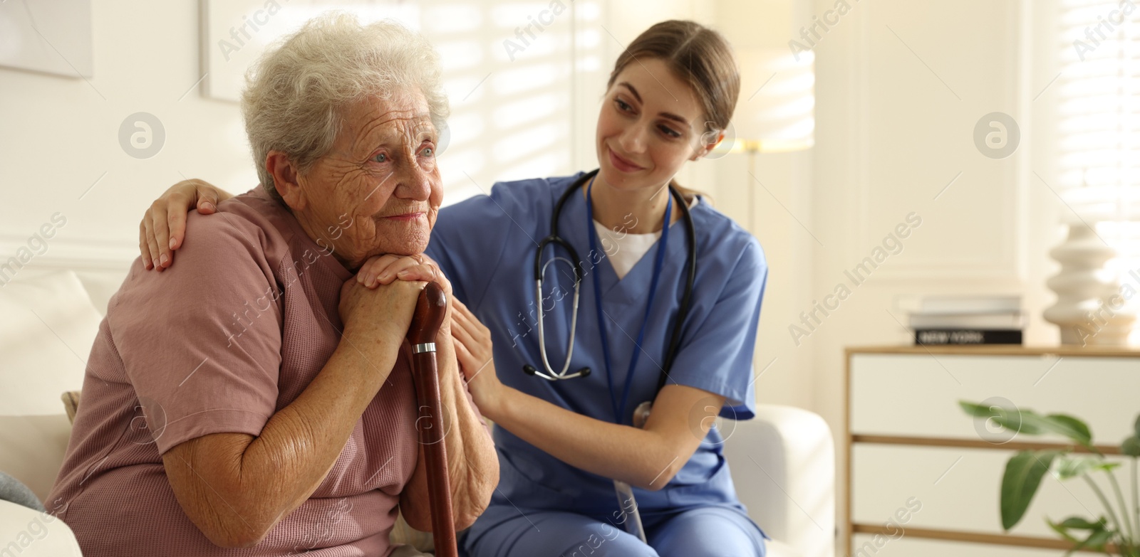 Photo of Caregiver supporting senior woman on sofa. Home health care service