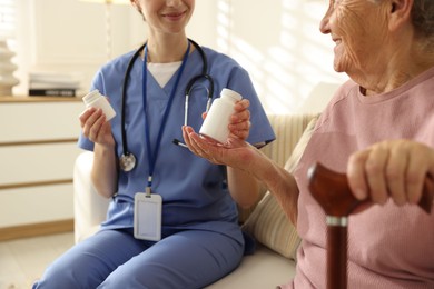 Photo of Caregiver giving pills to senior woman on sofa indoors, closeup. Home health care service