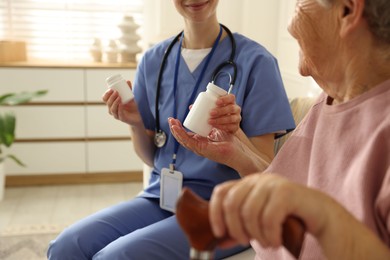 Photo of Caregiver giving pills to senior woman on sofa indoors, closeup. Home health care service