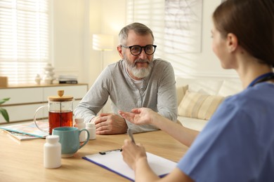 Caregiver examining senior man at table indoors. Home health care service