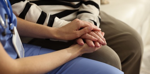 Photo of Caregiver supporting senior woman indoors, closeup. Home health care service