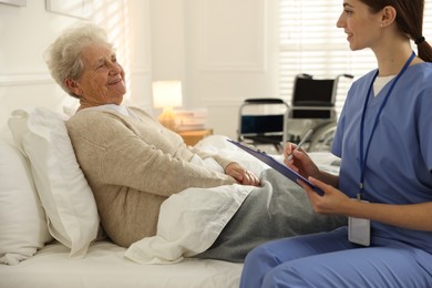 Caregiver examining senior woman on bed indoors. Home health care service