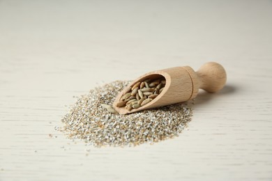 Photo of Pile of fresh rye bran and scoop with kernels on light wooden table