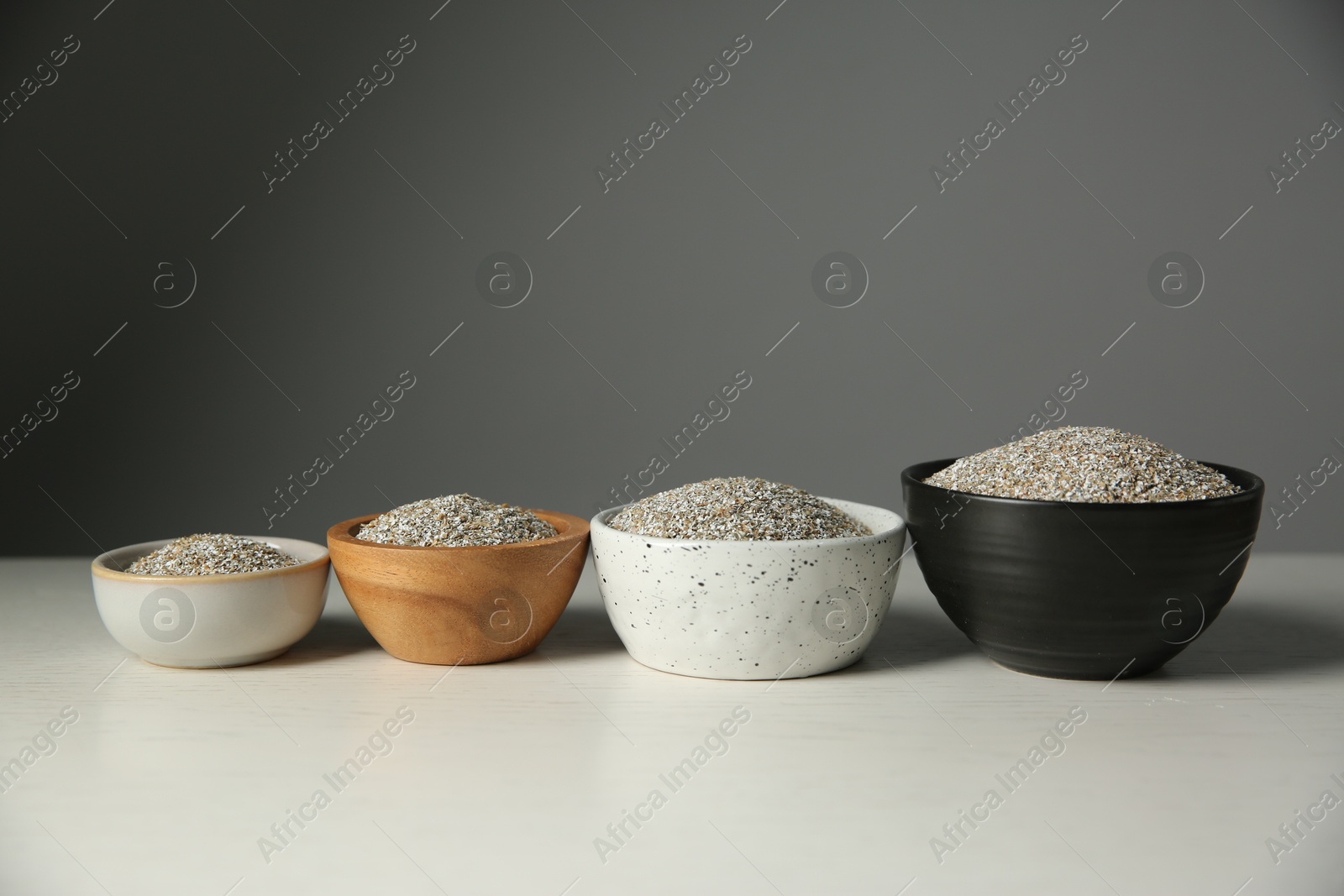 Photo of Fresh rye bran in bowls on light wooden table against grey wall