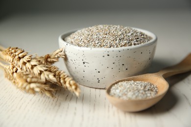 Photo of Fresh rye bran in bowl, spikelets and spoon on light wooden table, closeup