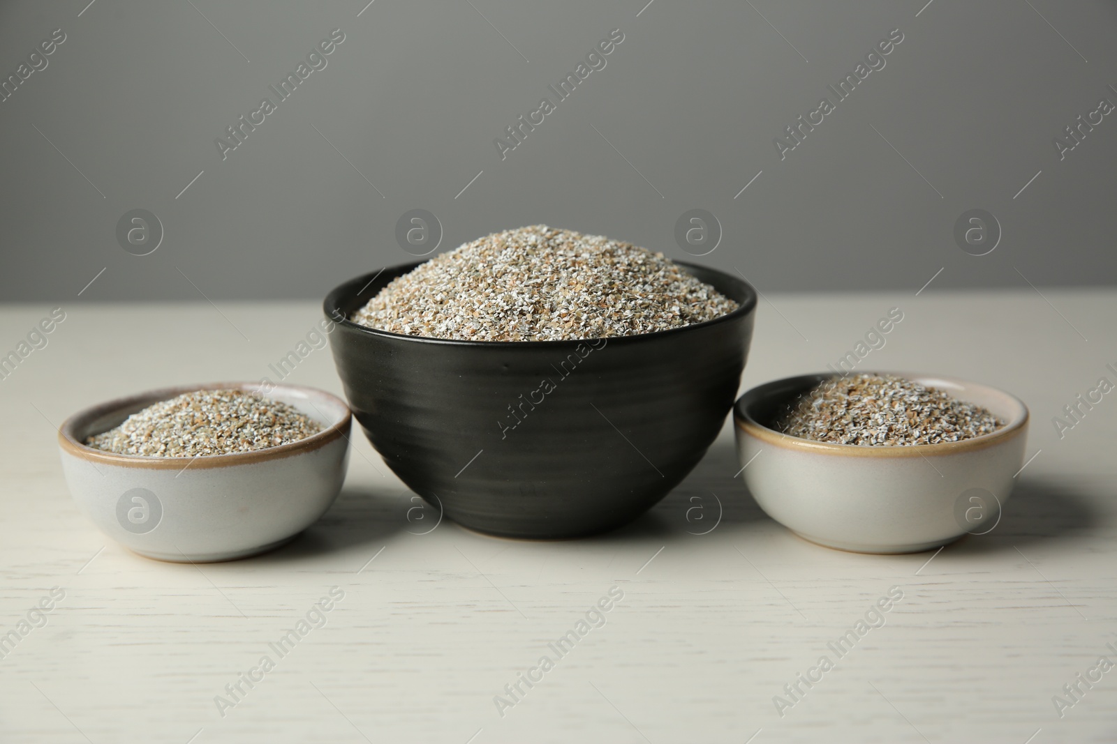 Photo of Fresh rye bran in bowls on light wooden table against grey wall