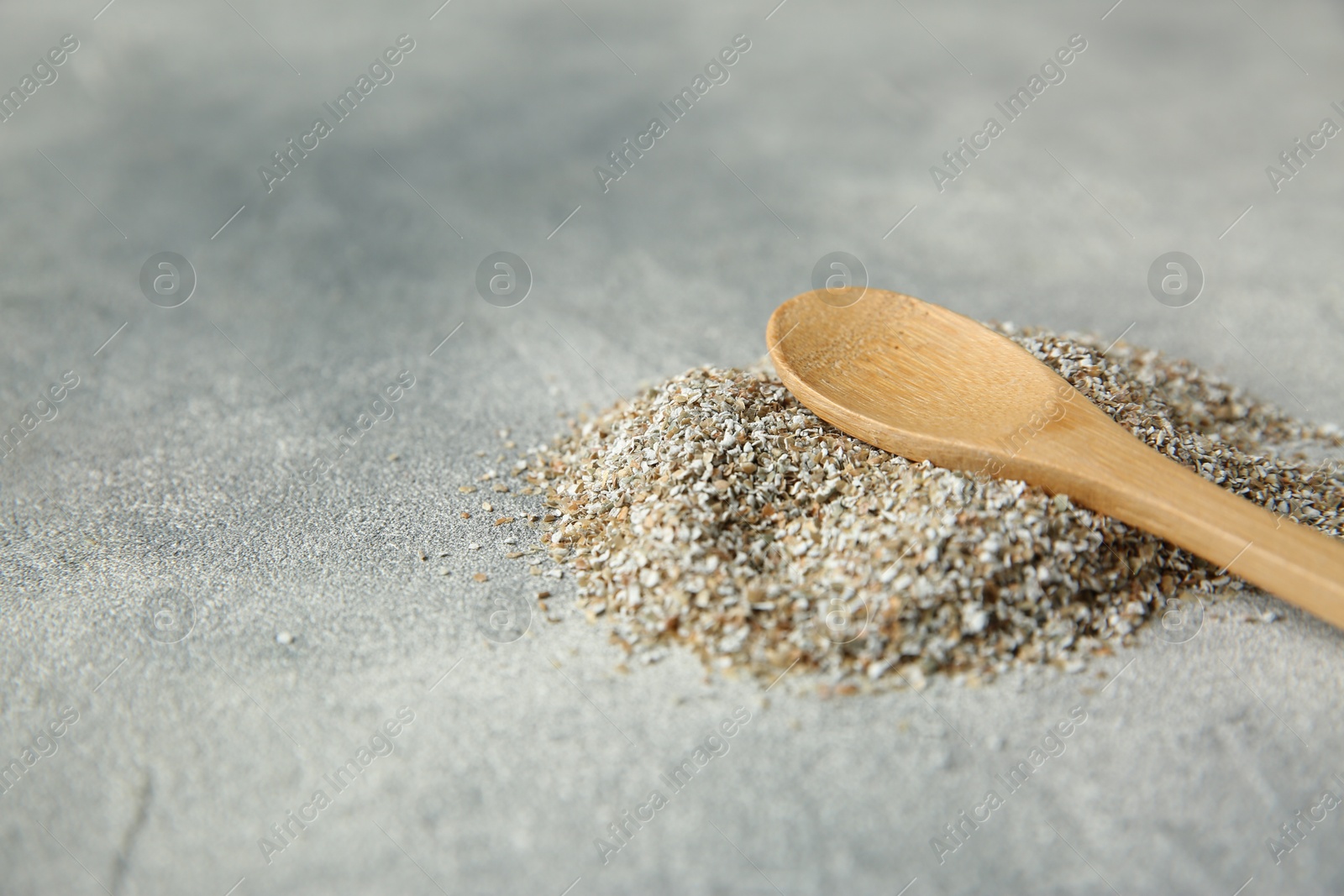 Photo of Pile of fresh rye bran and spoon on grey textured table, closeup. Space for text