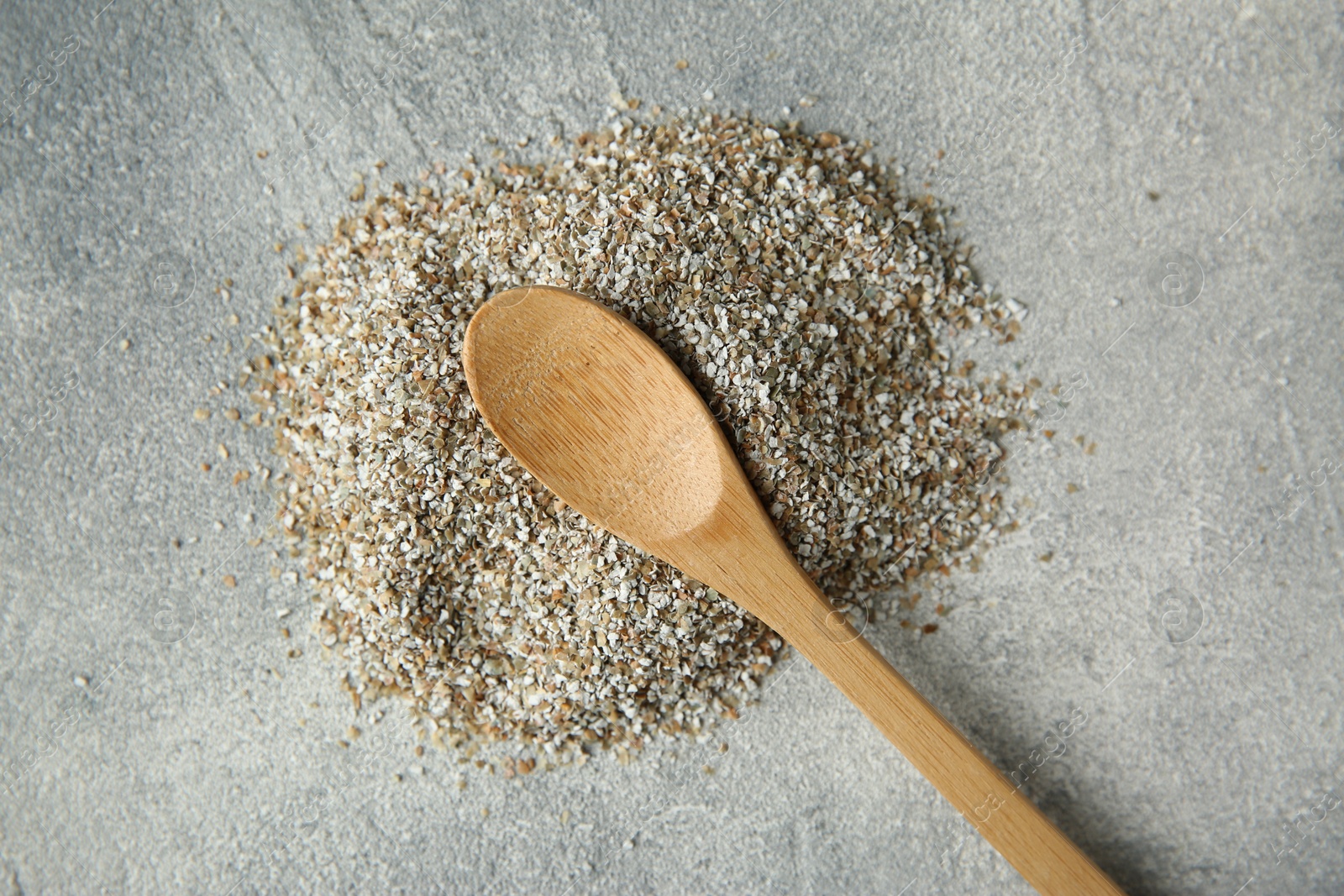 Photo of Pile of fresh rye bran and spoon on grey textured table, top view