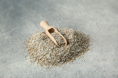 Photo of Pile of fresh rye bran and scoop on grey textured table, closeup