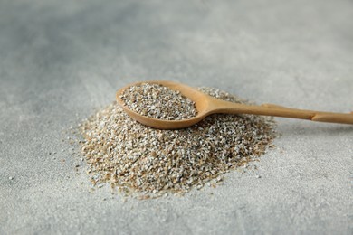 Photo of Pile of fresh rye bran and spoon on grey textured table, closeup