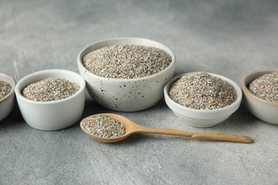 Photo of Fresh rye bran in bowls and spoon on grey textured table