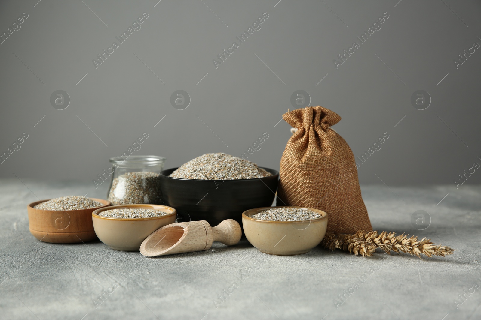 Photo of Fresh rye bran, scoop and spikelets on grey textured table