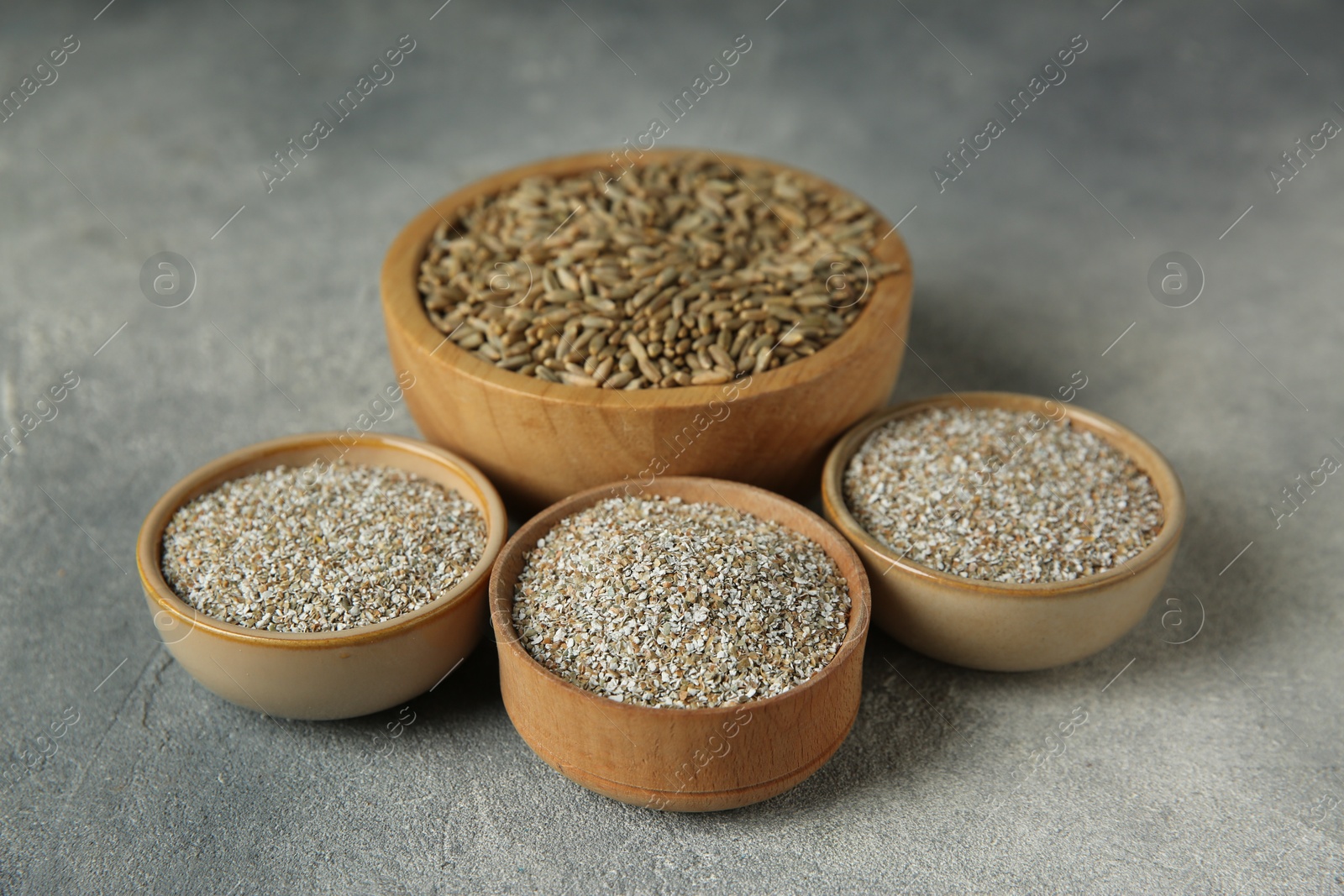 Photo of Fresh rye bran and kernels in bowls on grey textured table