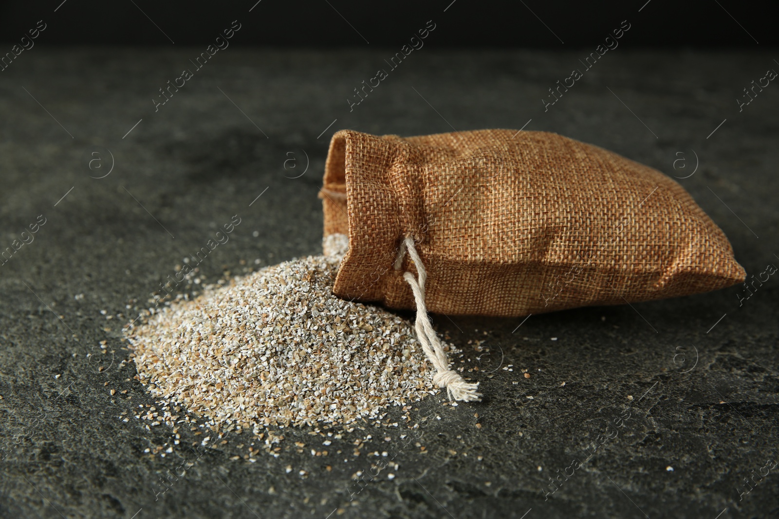 Photo of Sack with fresh rye bran on grey textured table, closeup