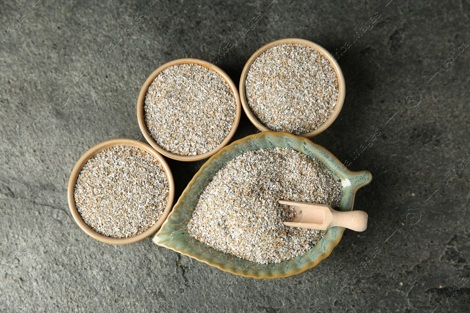 Photo of Fresh rye bran and scoop on grey textured table, flat lay