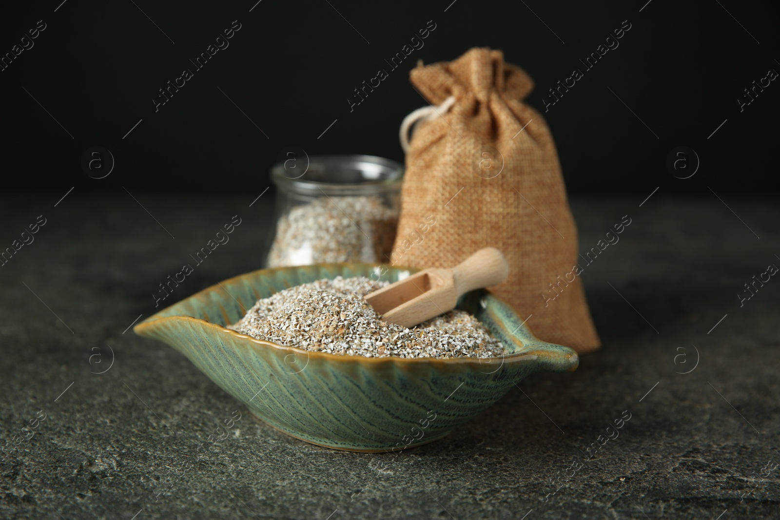 Photo of Fresh rye bran and scoop on grey textured table