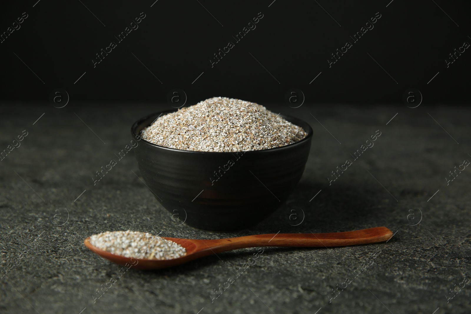 Photo of Fresh rye bran in bowl and spoon on grey textured table, closeup