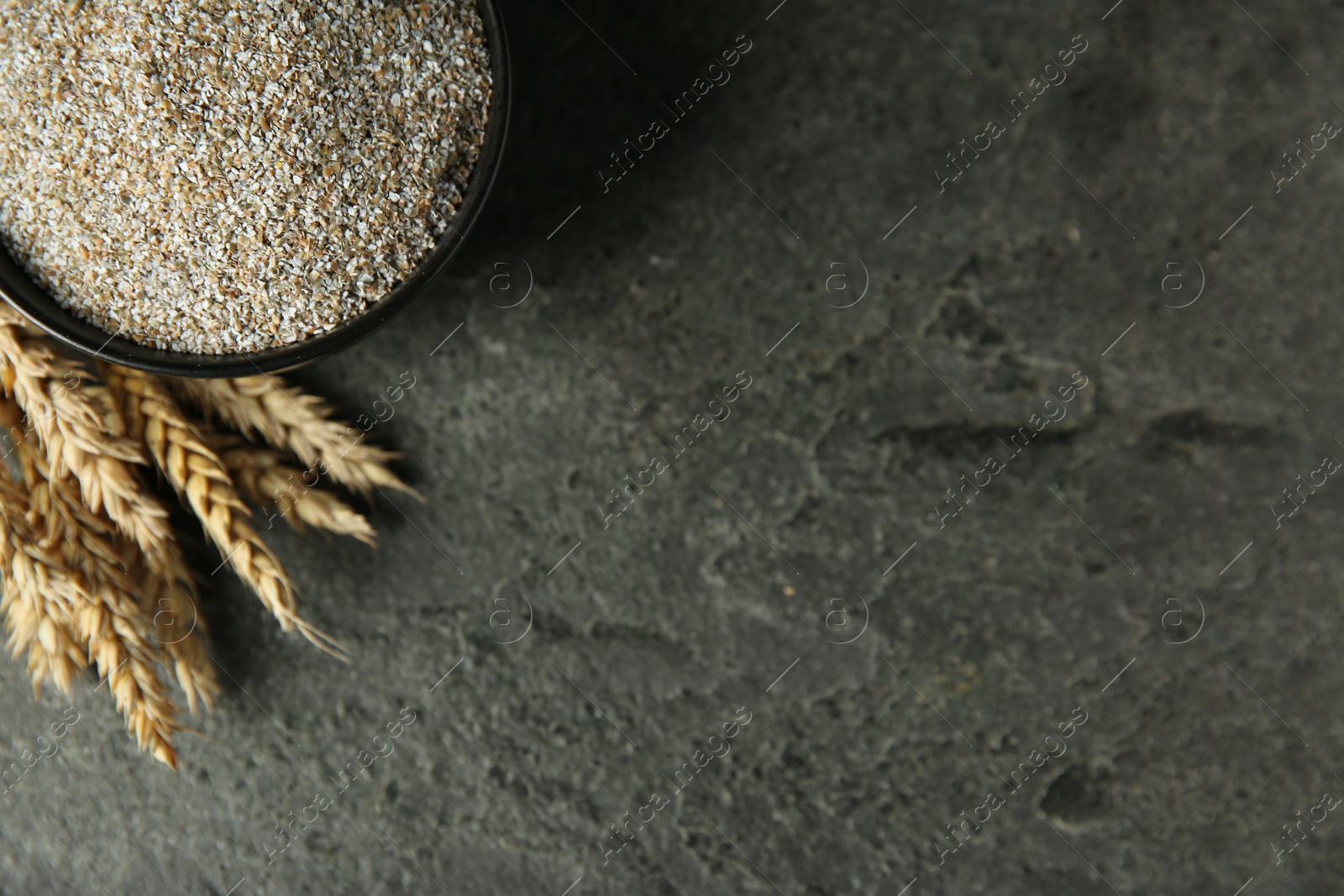 Photo of Fresh rye bran in bowl and spikelets on grey textured table, flat lay. Space for text