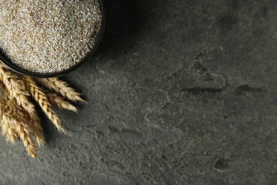 Photo of Fresh rye bran in bowl and spikelets on grey textured table, flat lay. Space for text