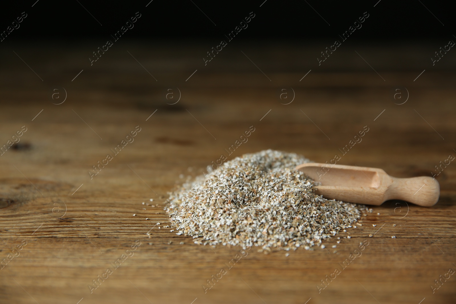 Photo of Pile of fresh rye bran and scoop on wooden table. Space for text