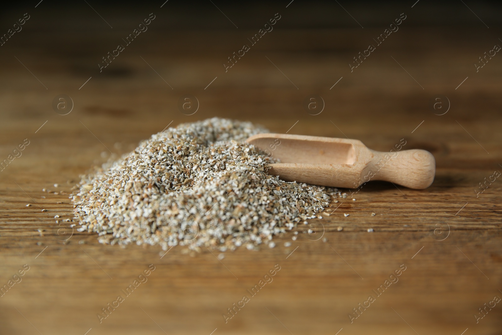 Photo of Pile of fresh rye bran and scoop on wooden table